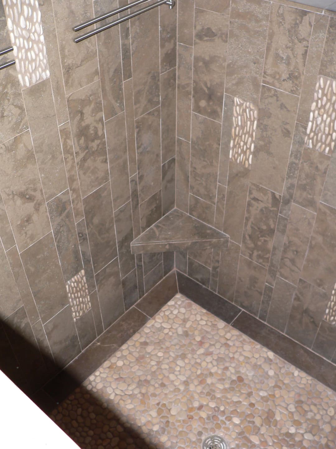 Stylish tiled shower corner with pebble floor and decorative wall features.