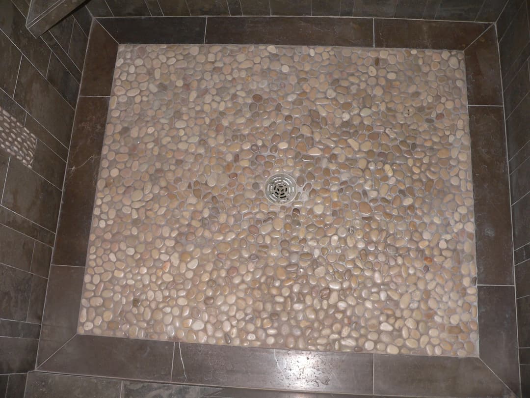 Natural stone pebble shower floor with a central drain and textured tile edges.