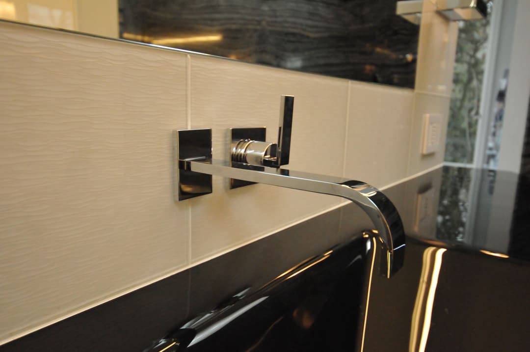 Modern chrome wall-mounted faucet in sleek bathroom design with textured tiles.