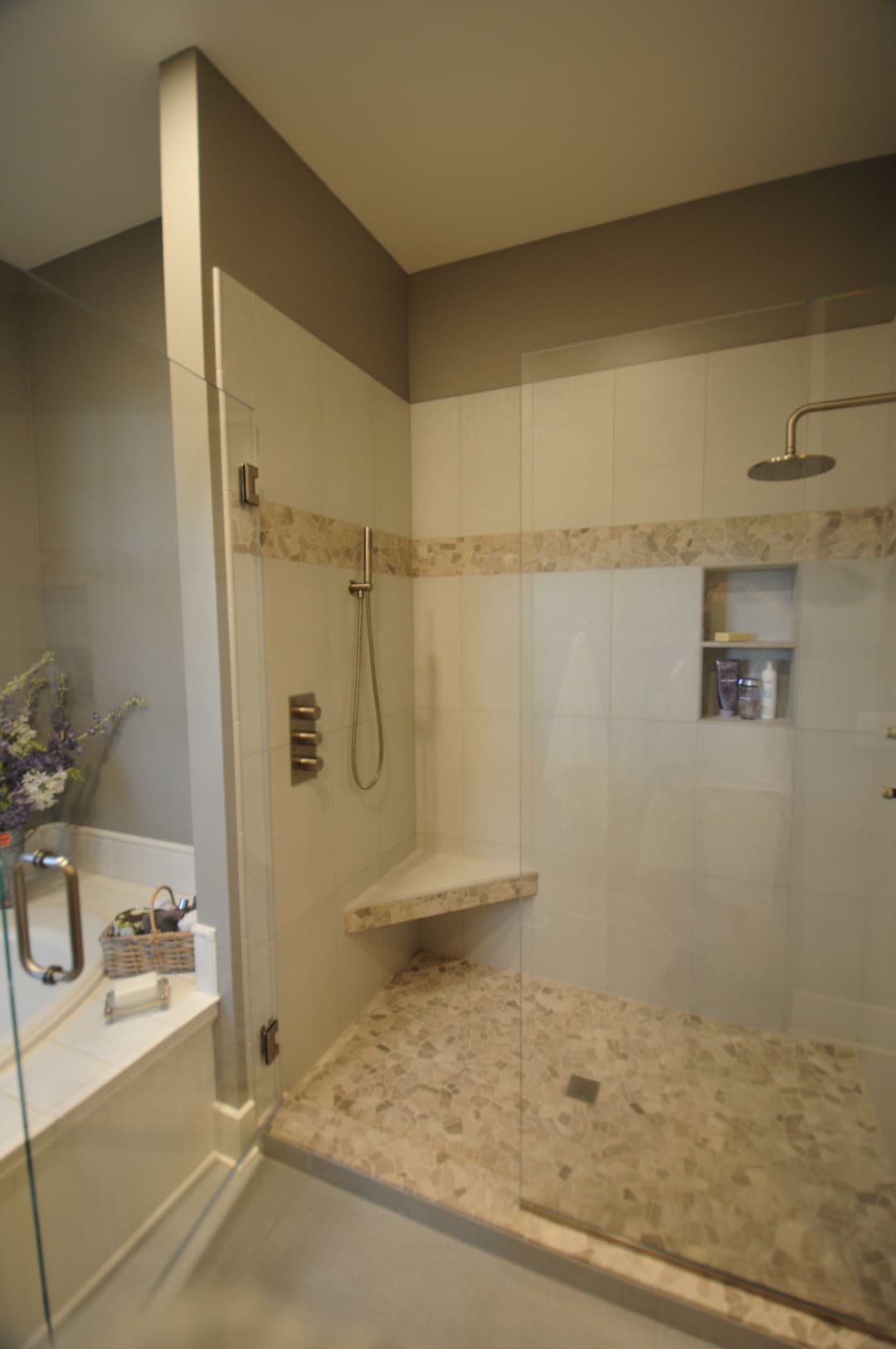 Modern glass shower with neutral tiles and built-in bench, featuring a luxurious rain showerhead.