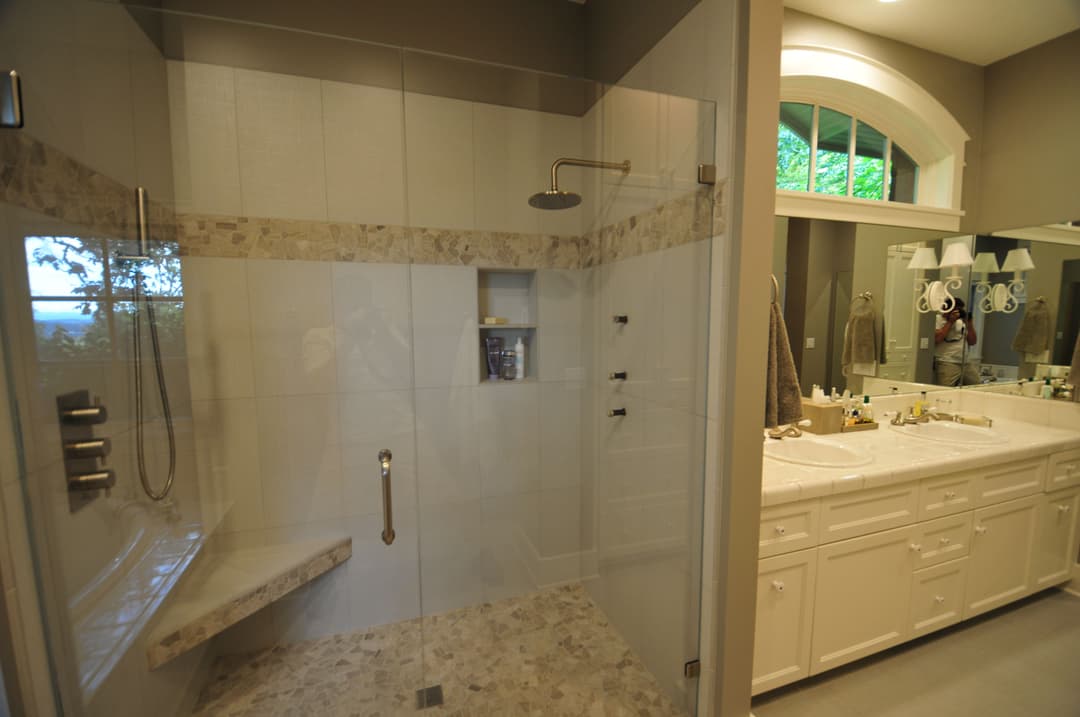 Modern bathroom with large glass shower, stone accents, and dual sinks. Bright and spacious layout.