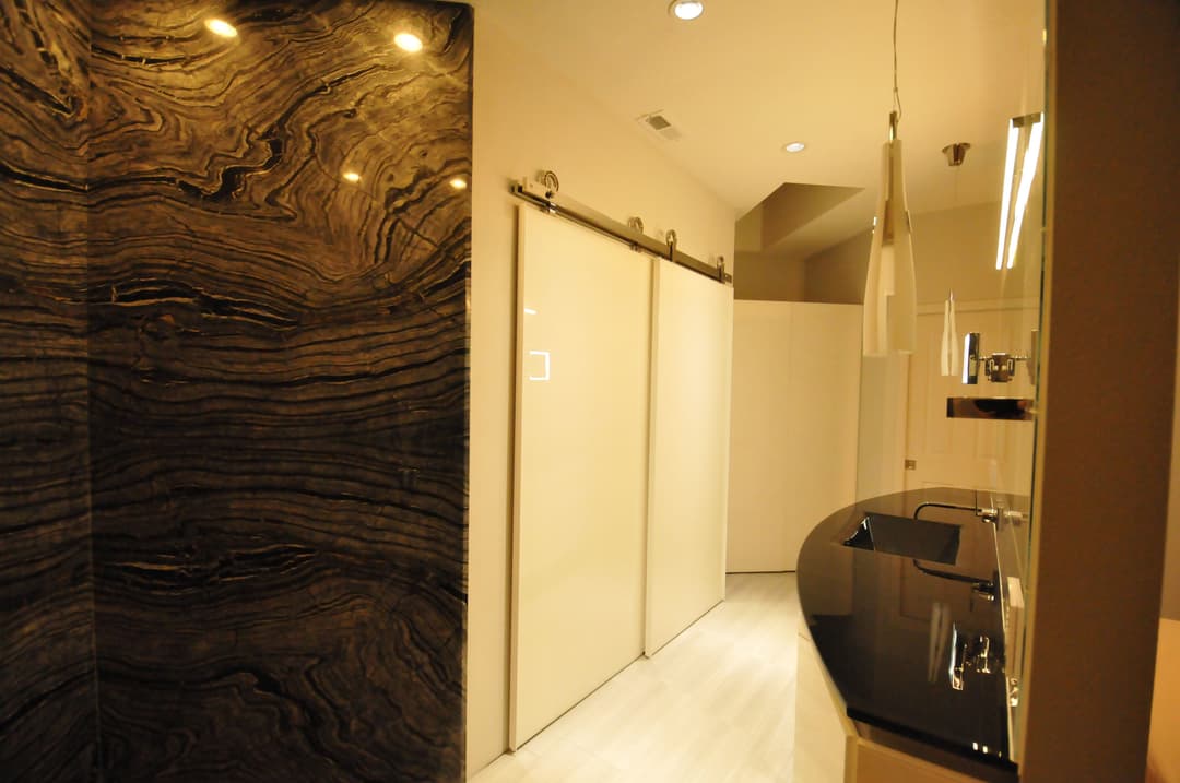 Modern bathroom with elegant black marble wall, sliding glass doors, and sleek vanity.