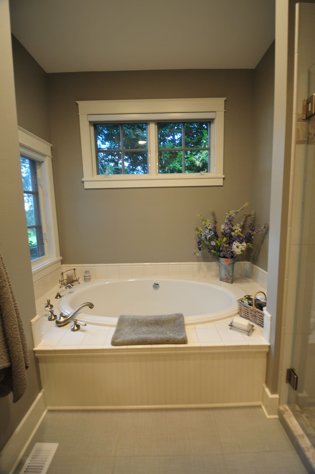 Luxurious bathroom with a white soaking tub, window view, and decorative flowers.