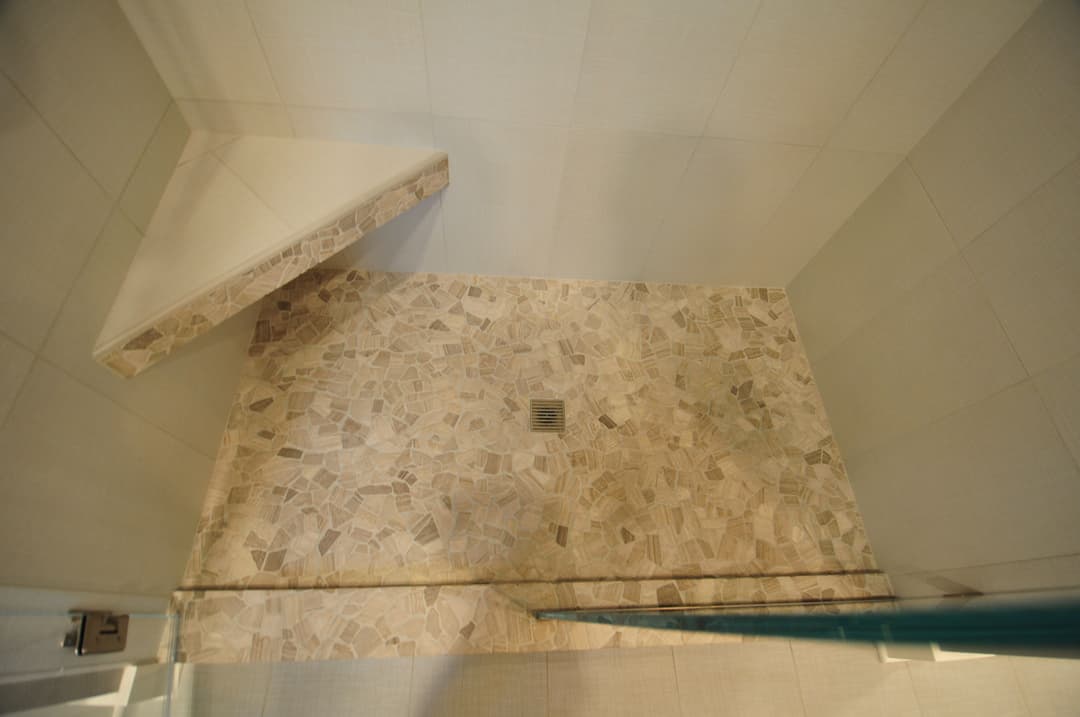 Modern walk-in shower with natural stone flooring and minimalist tile walls.