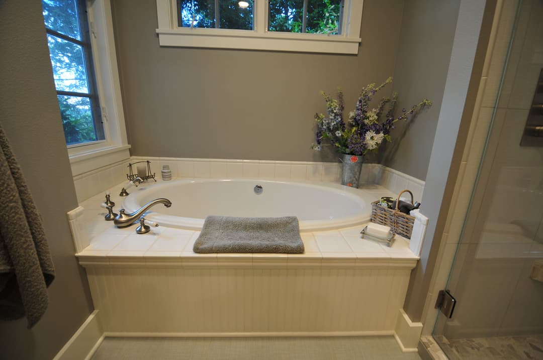 Elegant bathroom with a soaking tub, silver fixtures, and fresh floral arrangement.