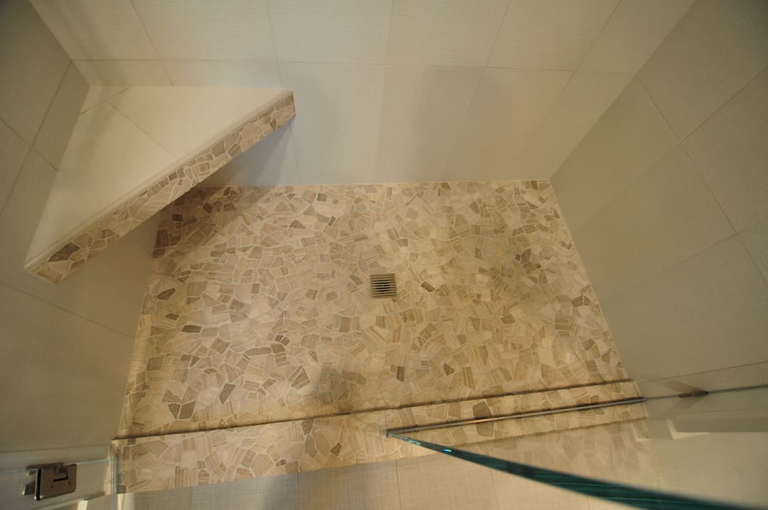 Modern shower featuring stone mosaic floor and sleek glass partition. Elegant bathroom design.