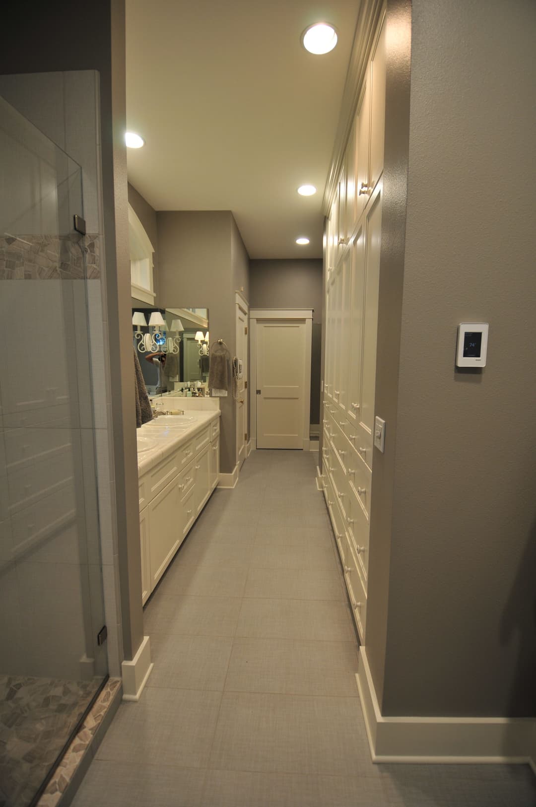 Modern bathroom hallway featuring white cabinetry and gray walls with ample lighting.