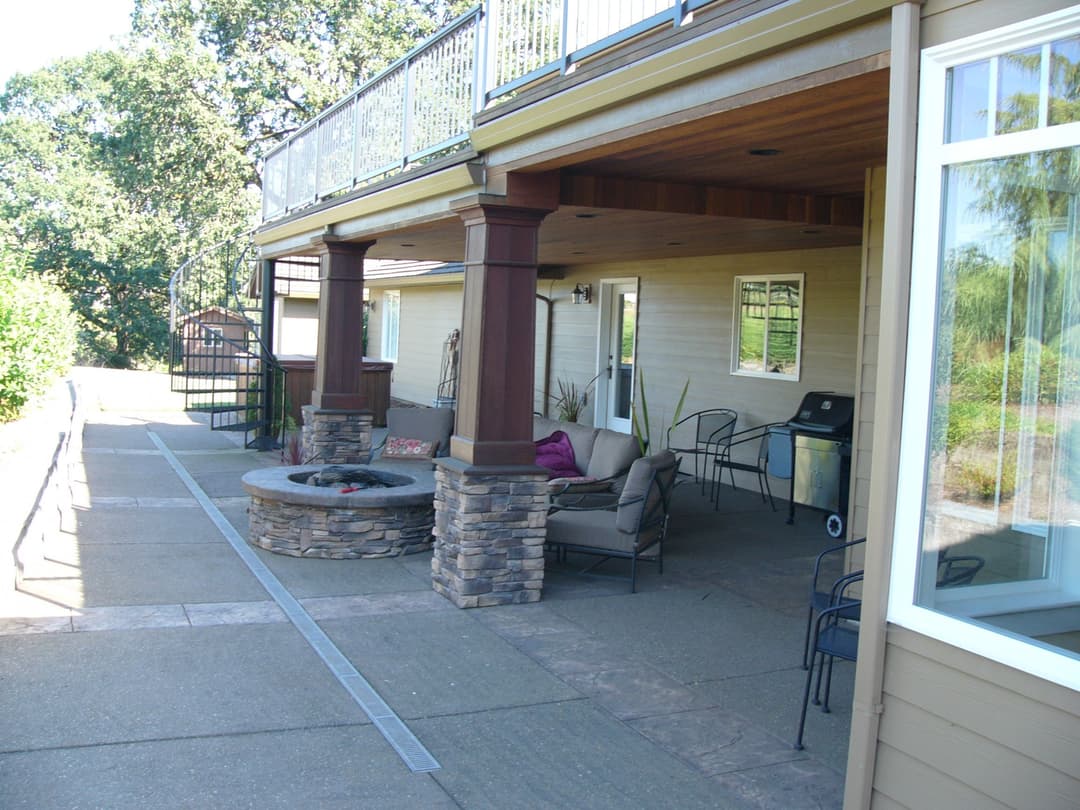Modern outdoor patio with stone fire pit, seating area, and expansive deck in serene landscape.