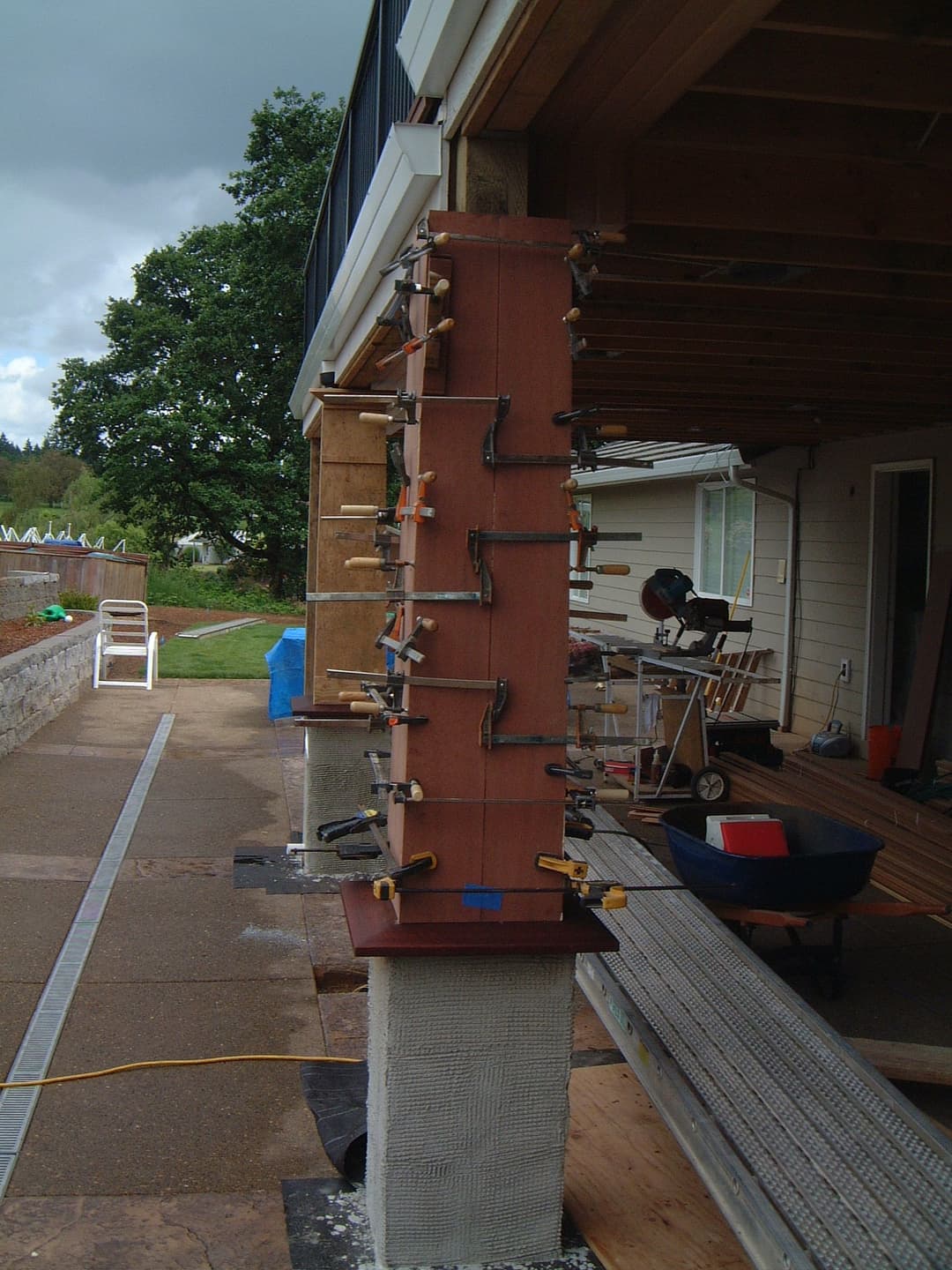 Woodworking project with clamps on a wooden post outdoors, showcasing renovation tools and workspace.