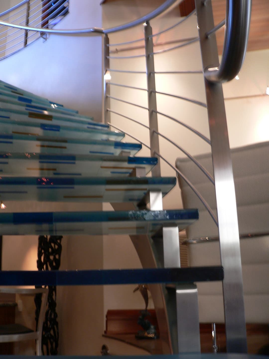 Modern glass and stainless steel staircase with blue accents in contemporary interior design.