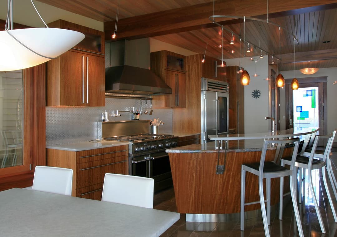 Modern kitchen with wood accents, stainless steel appliances, and sleek bar stools.