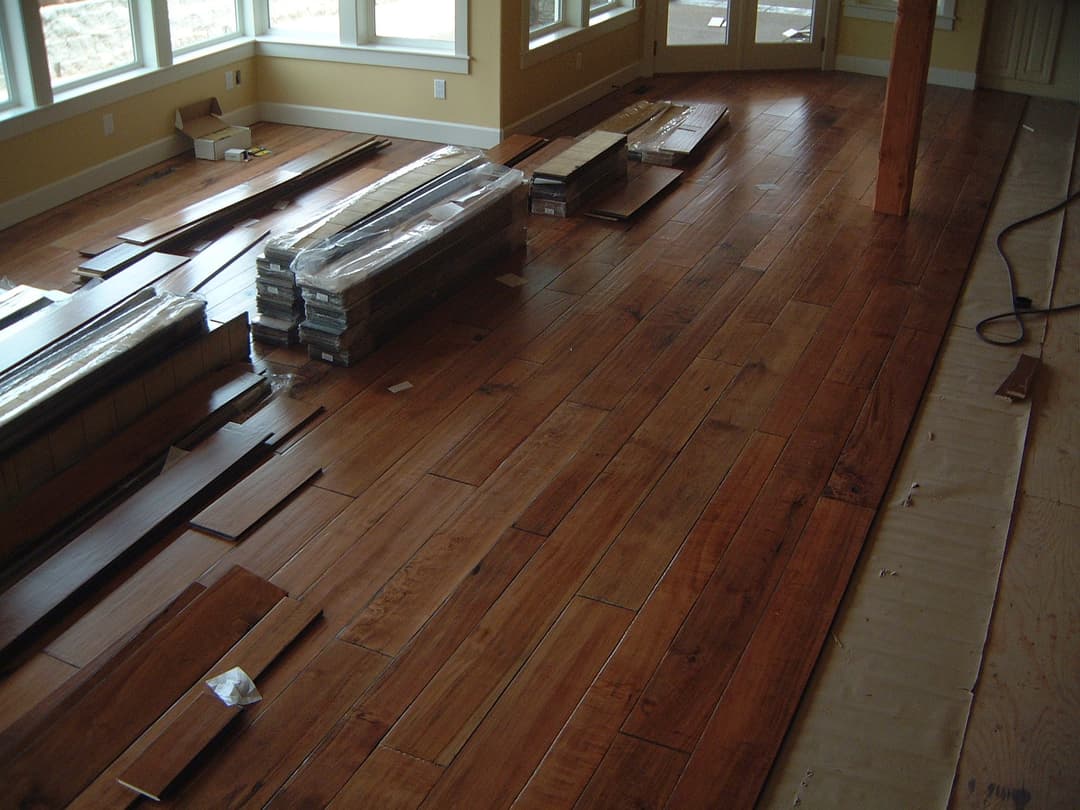 Hardwood flooring installation with stacked planks in a well-lit room.