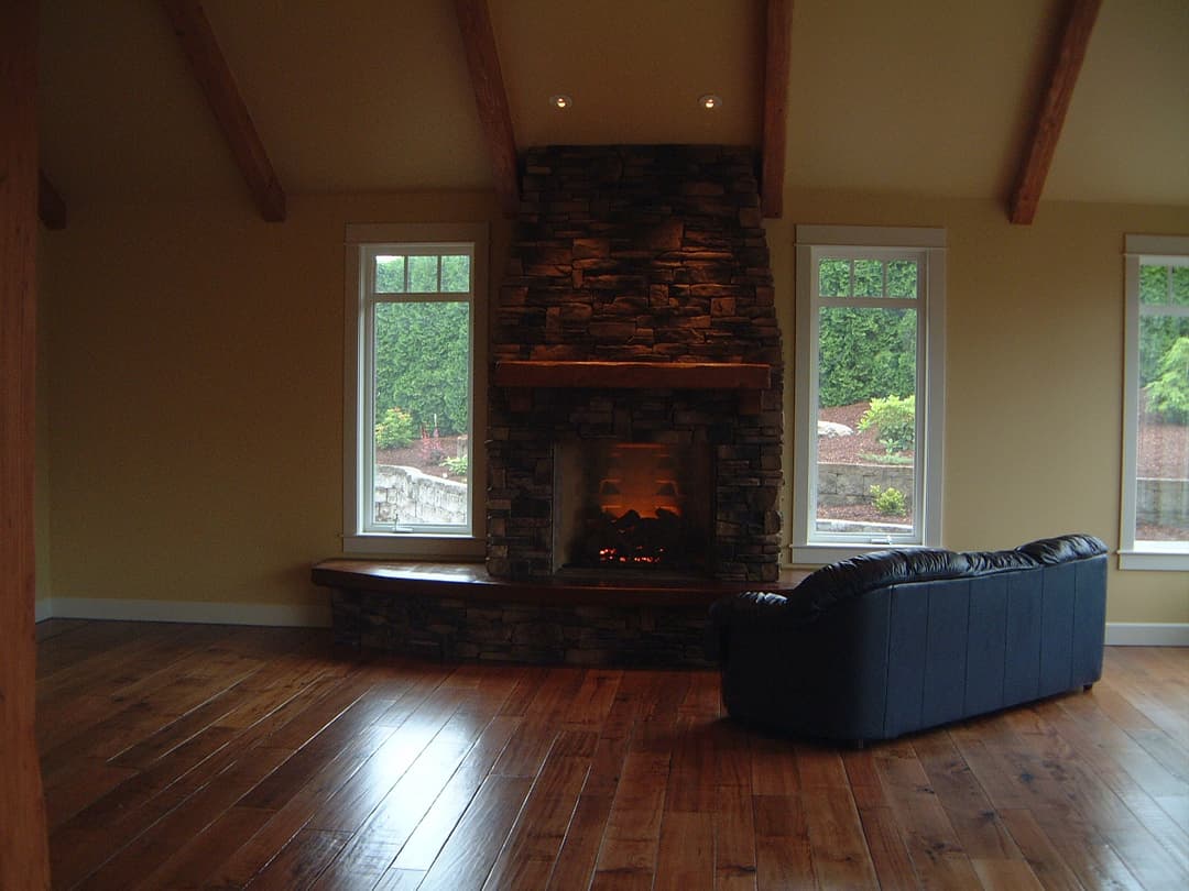 Modern living room with stone fireplace, wooden beams, and large windows. Comfortable seating area.