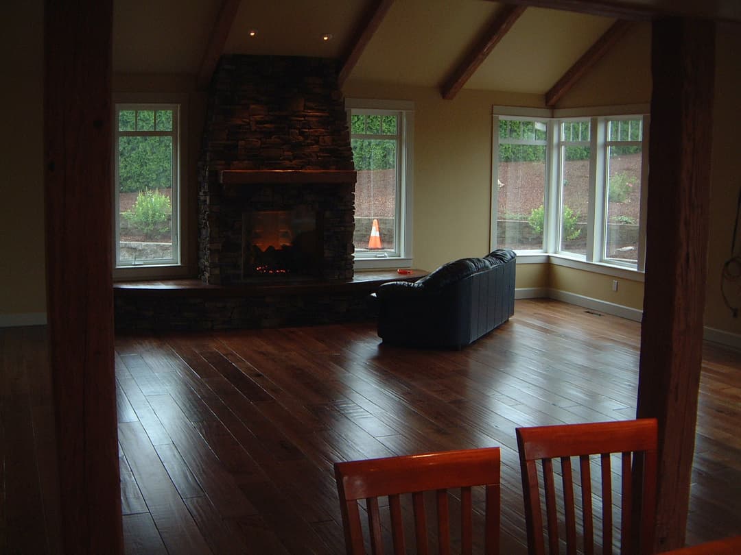 Spacious living room with a stone fireplace, large windows, and wooden flooring.