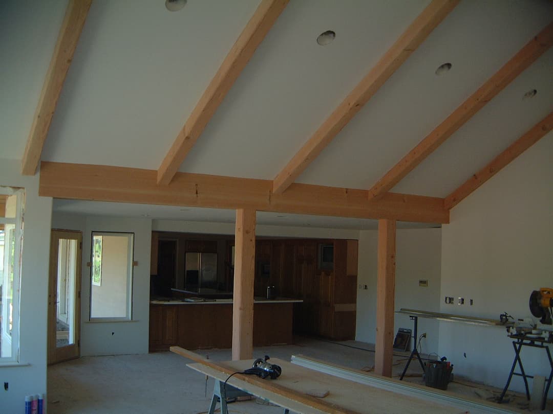 Modern interior with exposed wooden beams, spacious layout, and kitchen area in background.