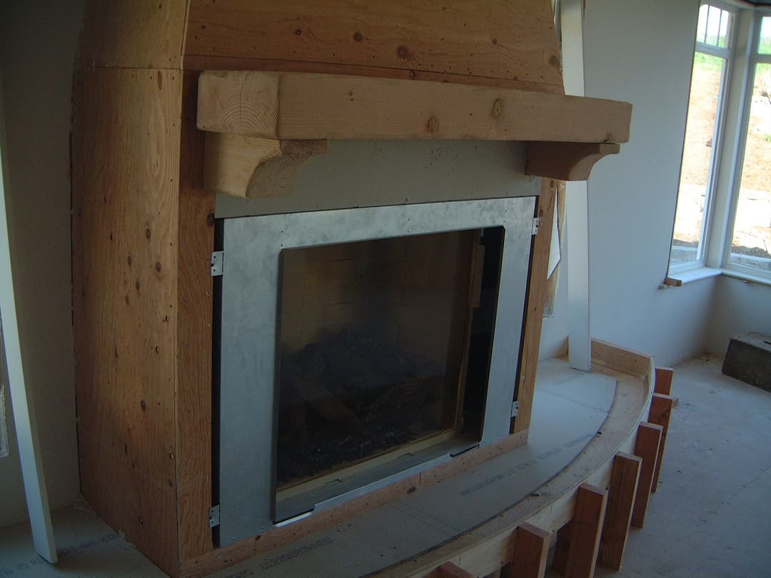 Modern fireplace installation with wooden mantle and unfinished surrounding structure.