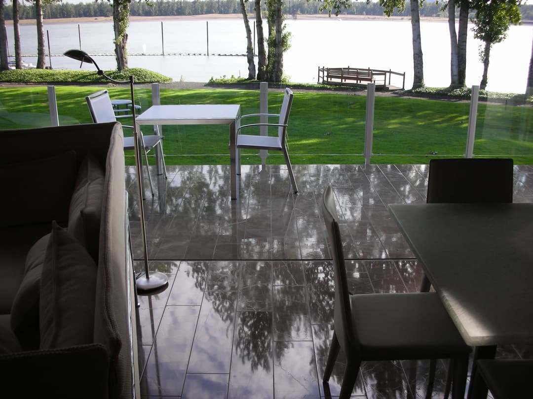 Modern outdoor patio with furniture overlooking a serene lakeside view and lush greenery.