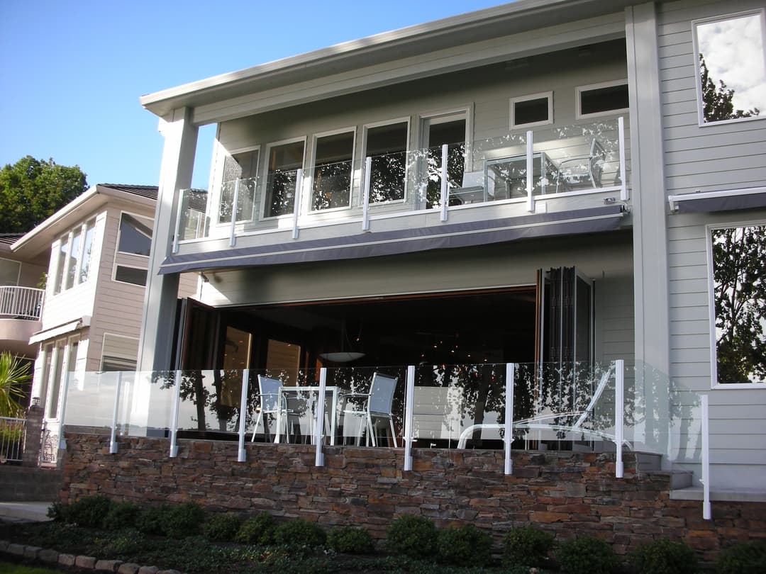 Modern home exterior with a balcony, glass railings, and outdoor dining area.