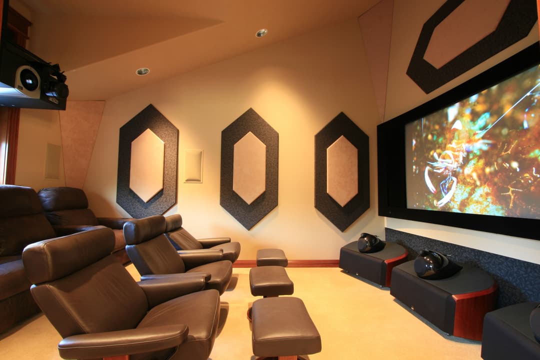 Home theater with plush seating, large screen, and acoustic wall panels for enhanced sound.