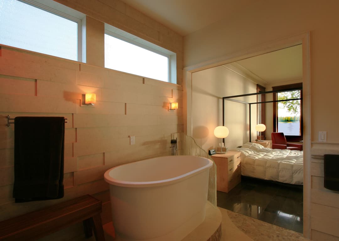 Modern bathroom with freestanding tub, warm lighting, and natural light from windows.