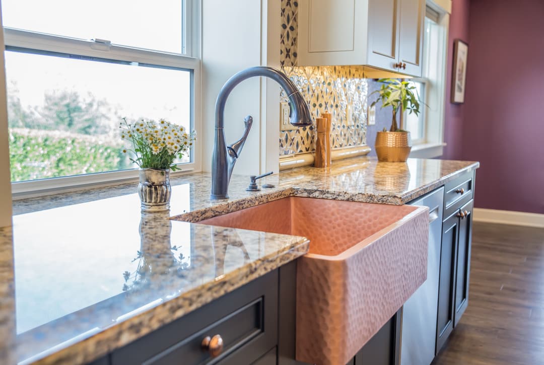 Modern kitchen featuring a copper farmhouse sink, granite countertop, and vibrant decor.