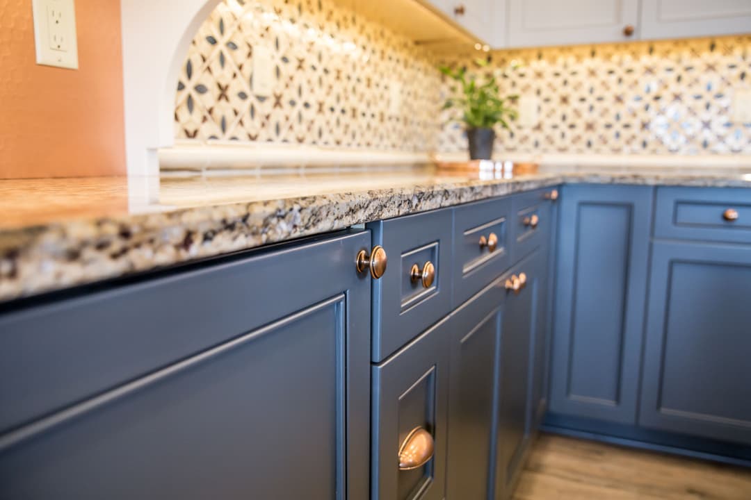 Blue kitchen cabinets with copper handles and a decorative tile backsplash. Elegant and modern design.