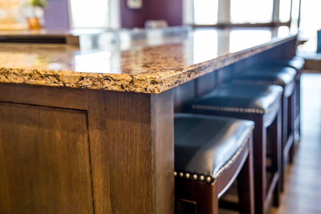 Granite countertop on wooden kitchen island with black leather stools. Modern kitchen design.