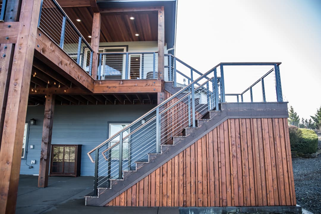 Modern wooden deck with stylish metal railing and staircase leading to a house exterior.