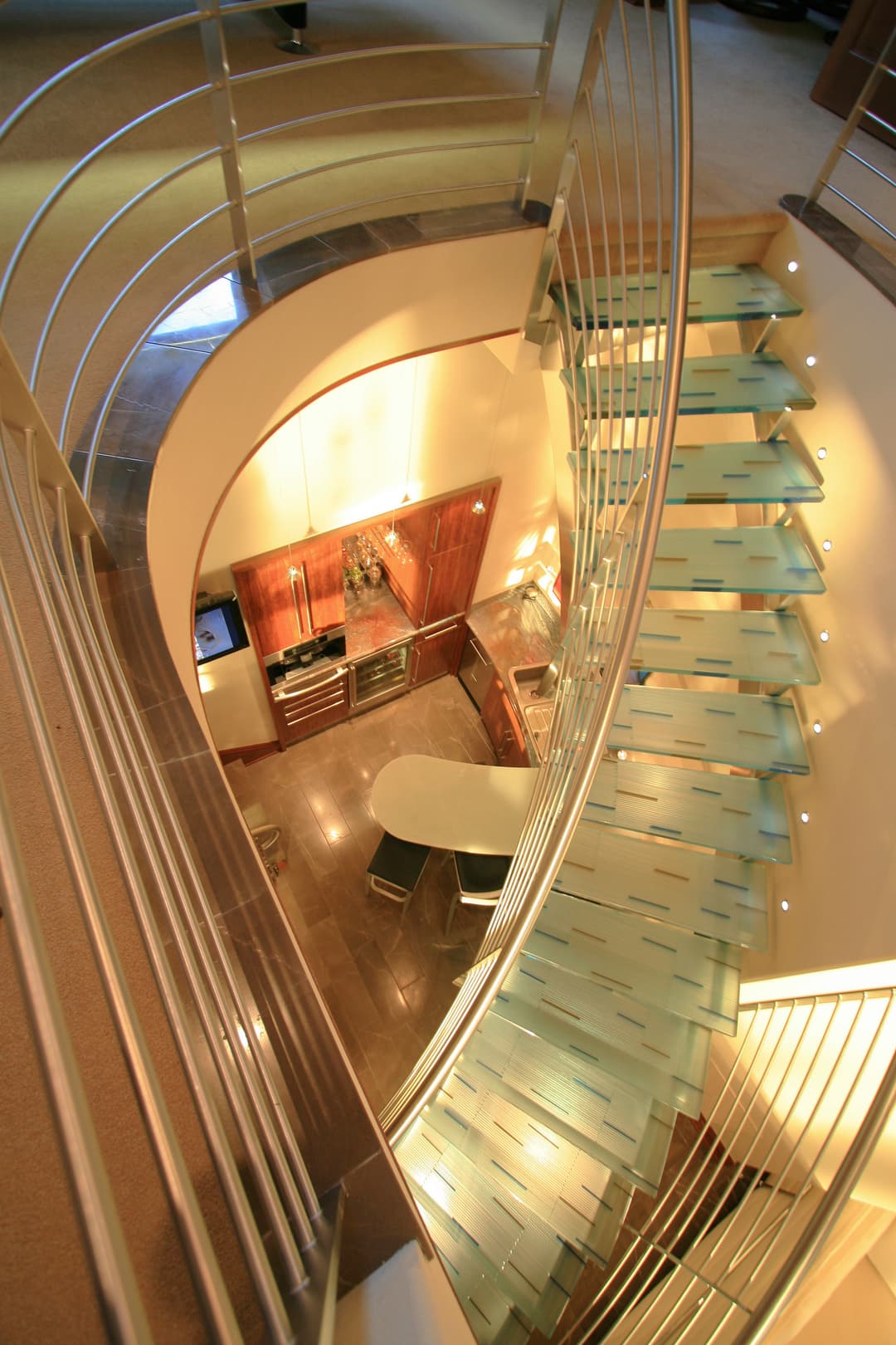Modern glass staircase with curved design, leading to a stylish kitchen below.