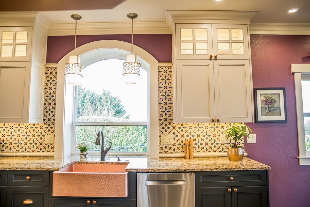 Modern kitchen with white cabinetry, copper sink, and stylish pendant lights above a granite countertop.