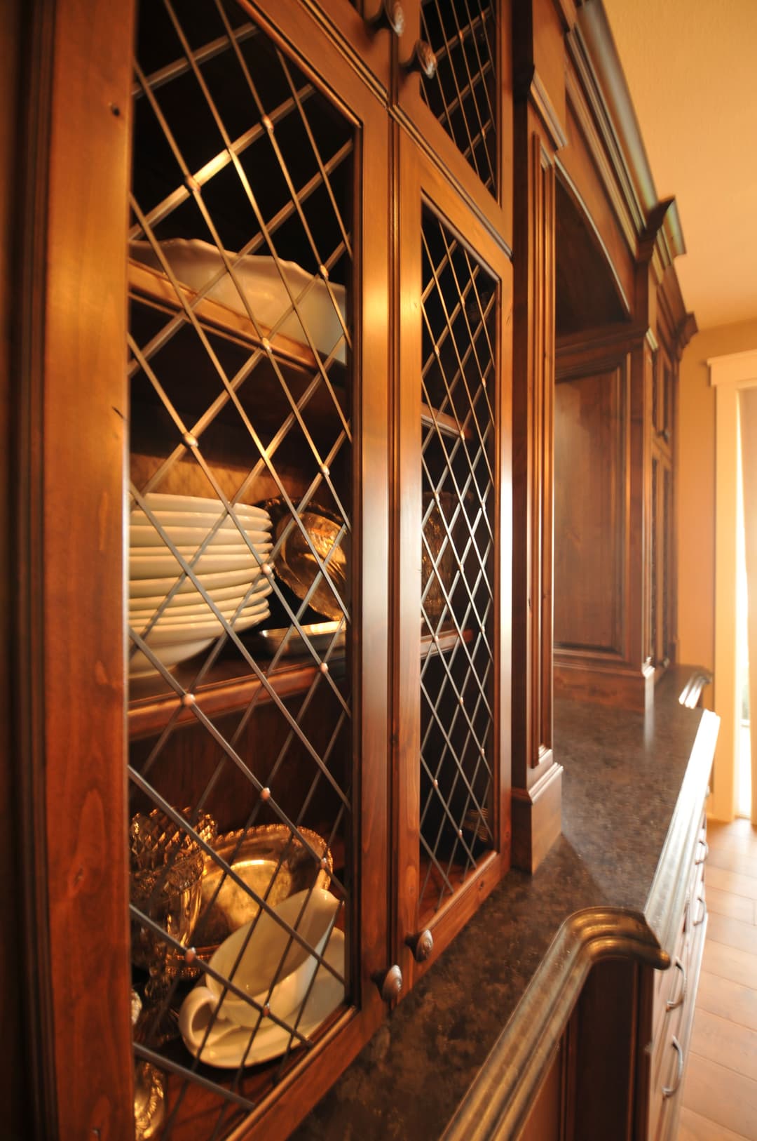 Elegant wooden kitchen cabinet with glass doors showcasing white plates and decorative items.