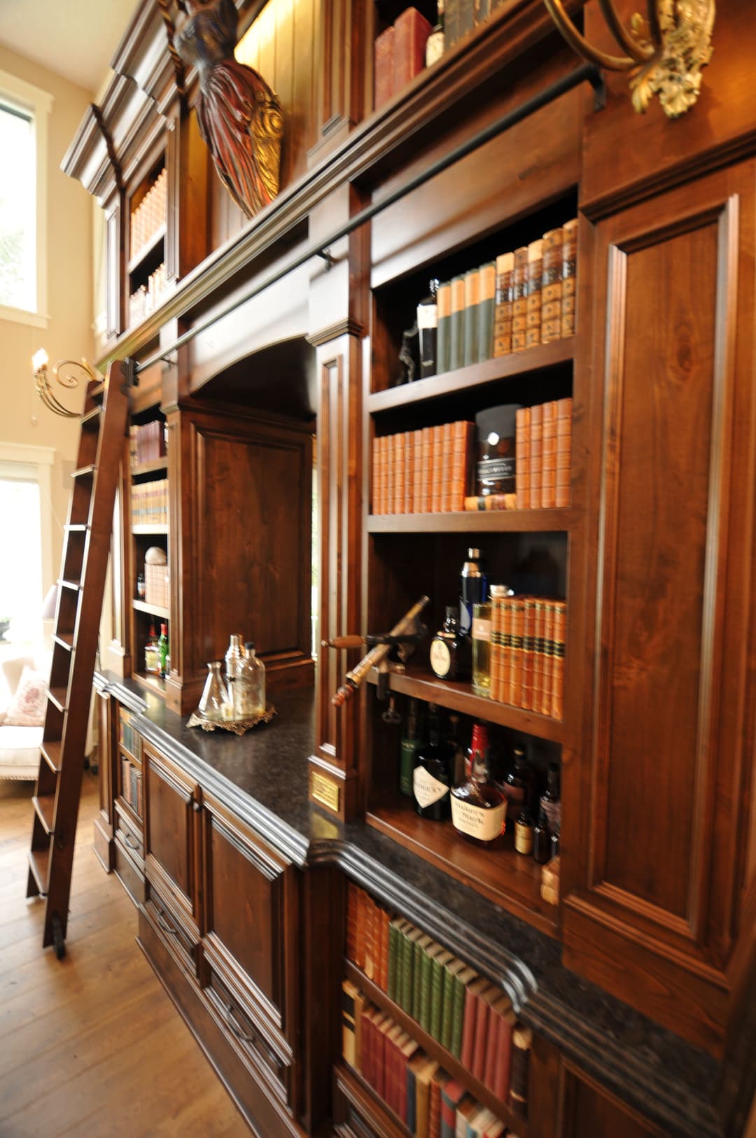 Elegant wooden library with bookshelves, a ladder, and a bar area featuring various bottles.