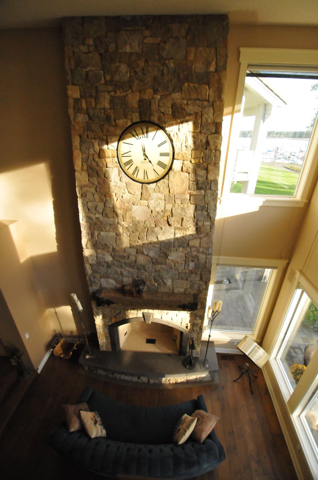 Elegant stone fireplace with large clock in a cozy living room, featuring natural light.