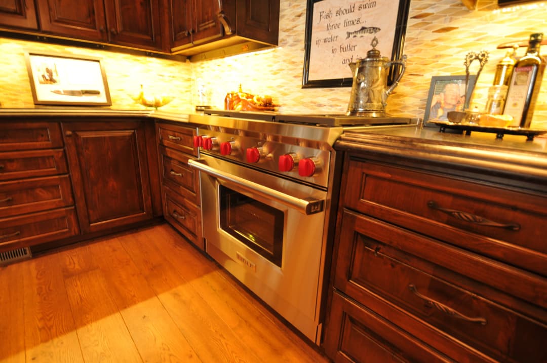 Modern kitchen with stainless steel range, red knobs, and wooden cabinetry. Warm lighting accents.