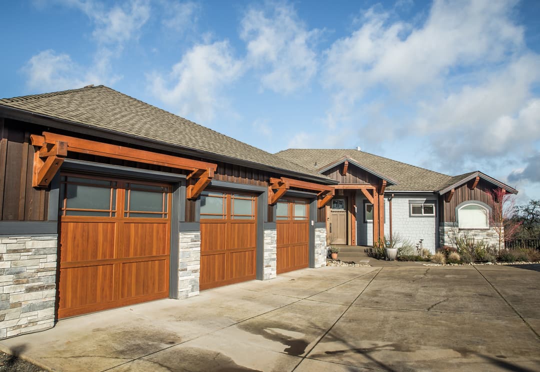 Modern home with stone accents and wooden garage doors under a blue sky.