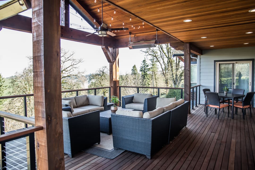 View of a modern outdoor patio with seating, dining area, and lush greenery in the background.