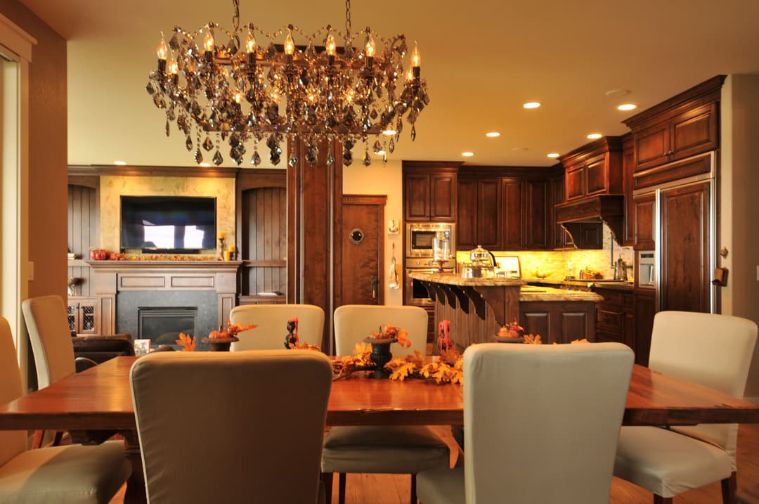 Elegant dining room featuring a chandelier, wooden table, and modern kitchen in warm tones.