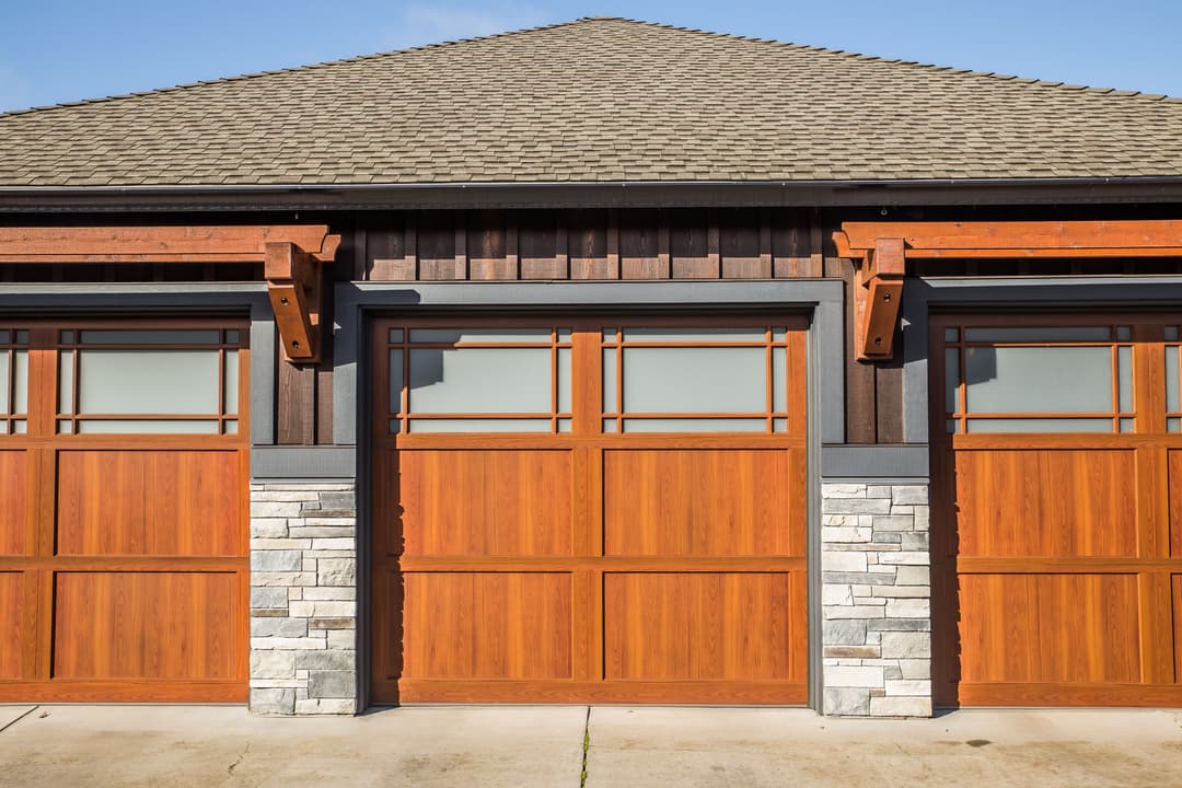 Contemporary wooden garage doors with stone accents under a textured roof.