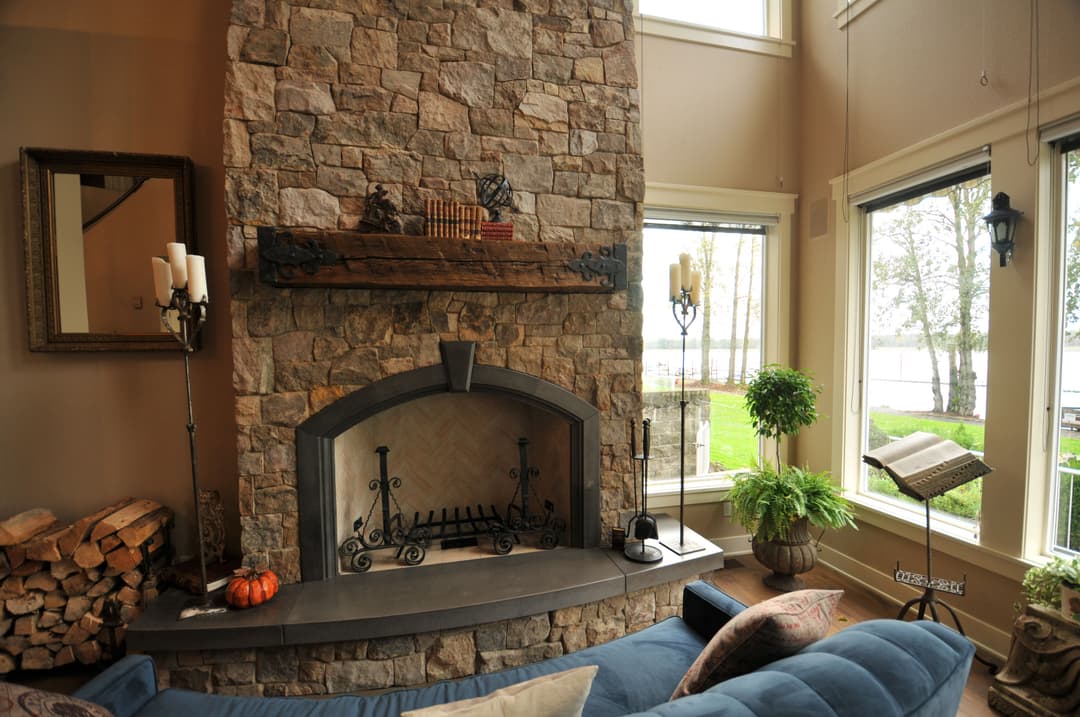 Cozy living room with stone fireplace, large windows, and rustic decor overlooking a lake.
