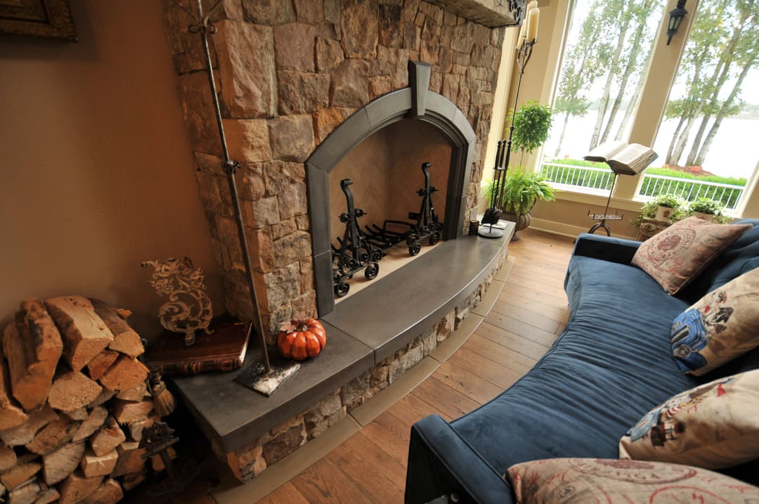Cozy living room with a stone fireplace, blue sofa, and lake view through large windows.