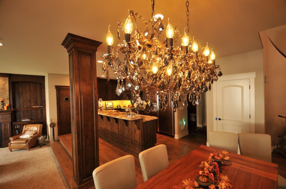 Elegant chandelier in a warmly decorated dining area with wooden accents and cozy kitchen view.