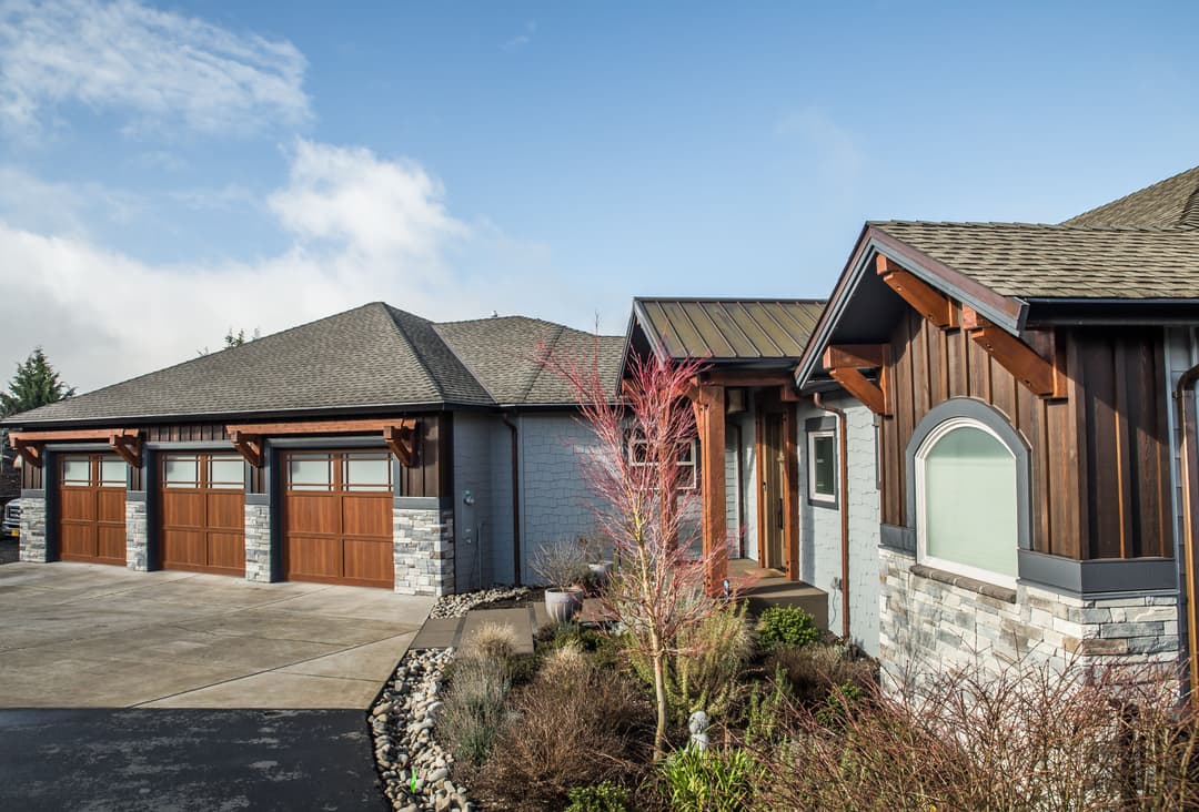 Modern home exterior with stone accents, wooden garage doors, and landscaped front yard.