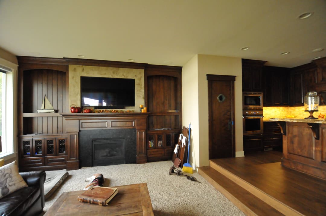 Cozy living room with dark wood accents, fireplace, and modern kitchen in background.