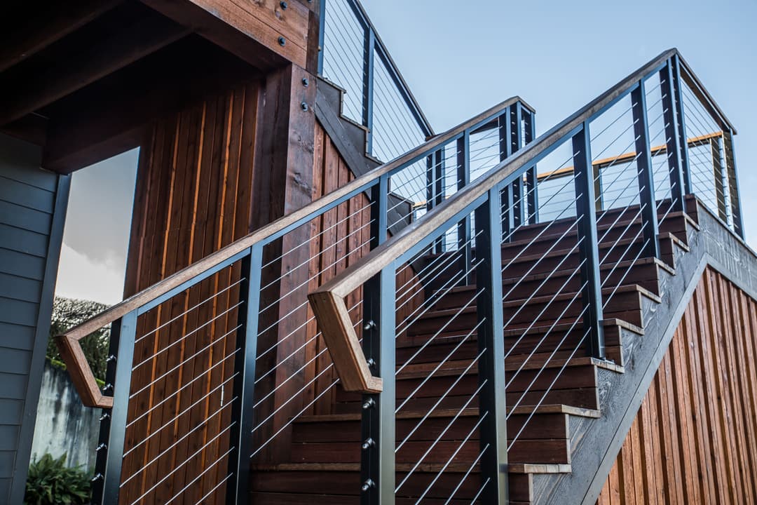 Modern wooden staircase with metal railing and cable details, leading to an upper walkway.