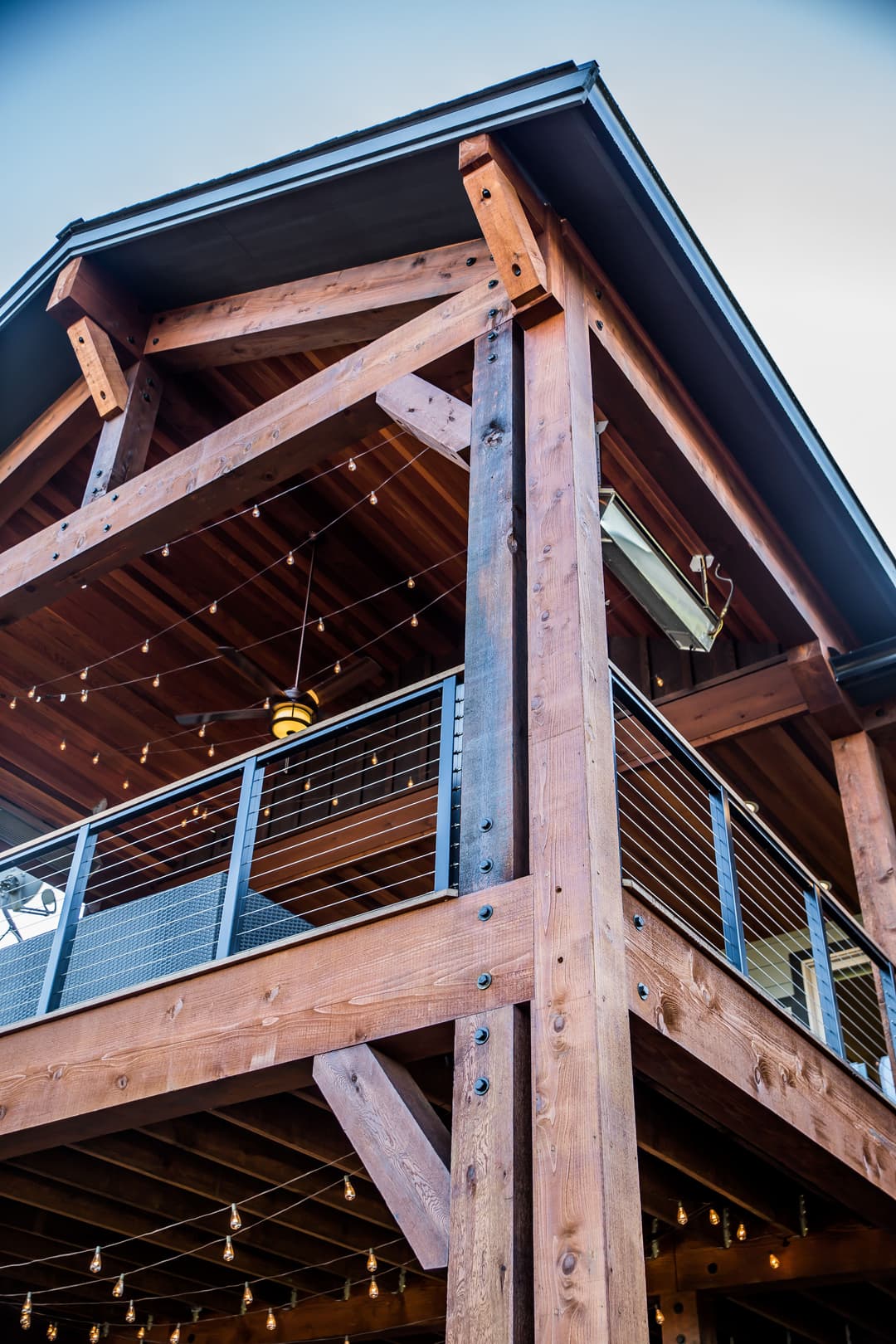 Sturdy wooden porch structure with string lights and modern railings against a blue sky.