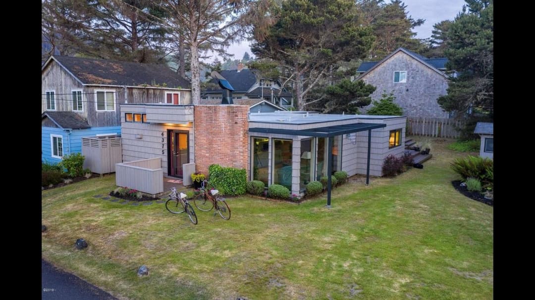 Modern house with unique architecture, surrounded by trees and two bicycles in the yard.