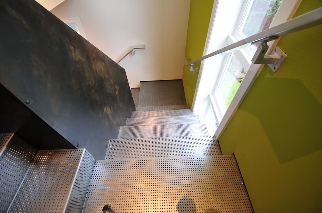 Metal staircase leading down to a bright room with green walls and large windows.