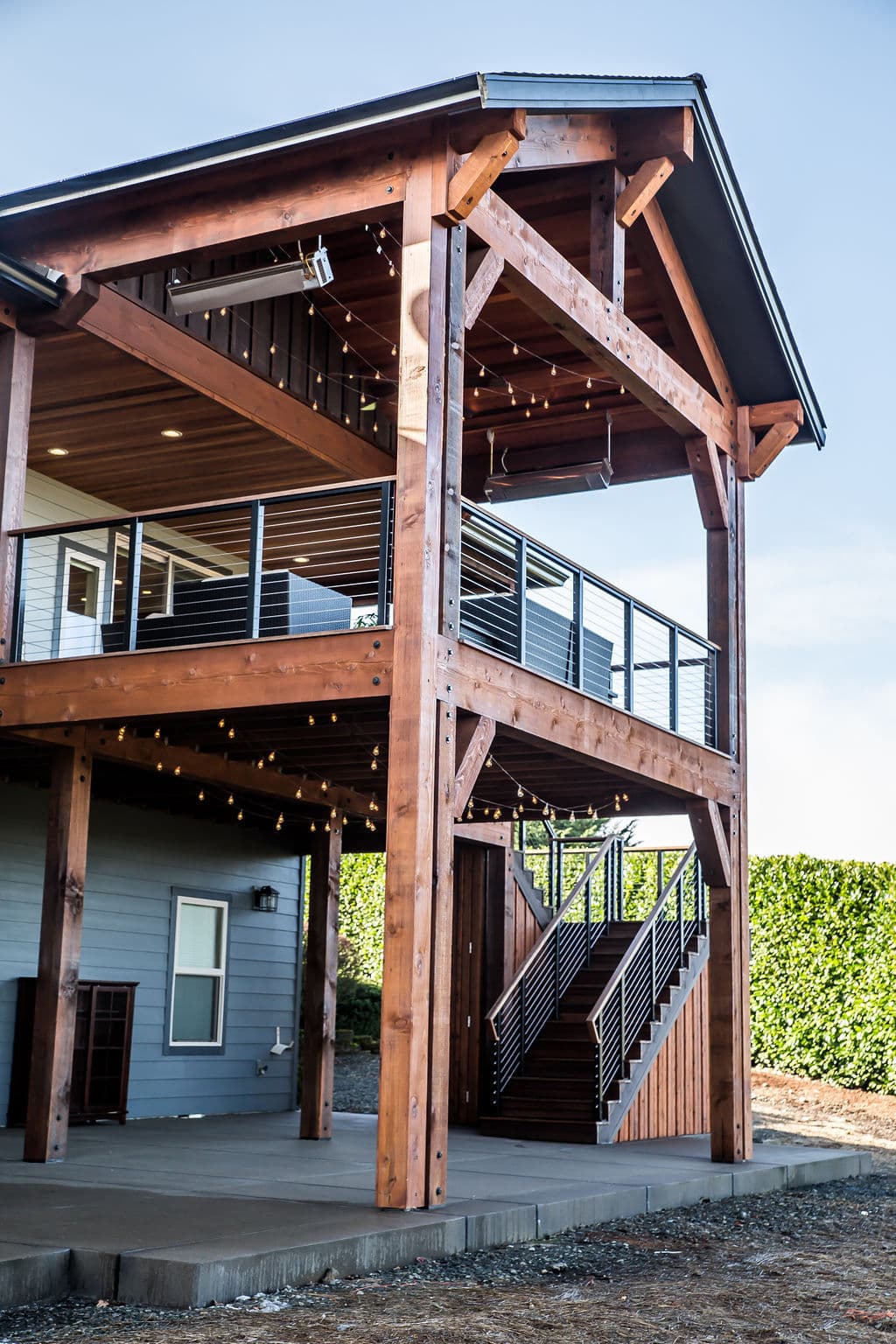 Modern two-story home with wooden beams, balcony, and outdoor lighting.