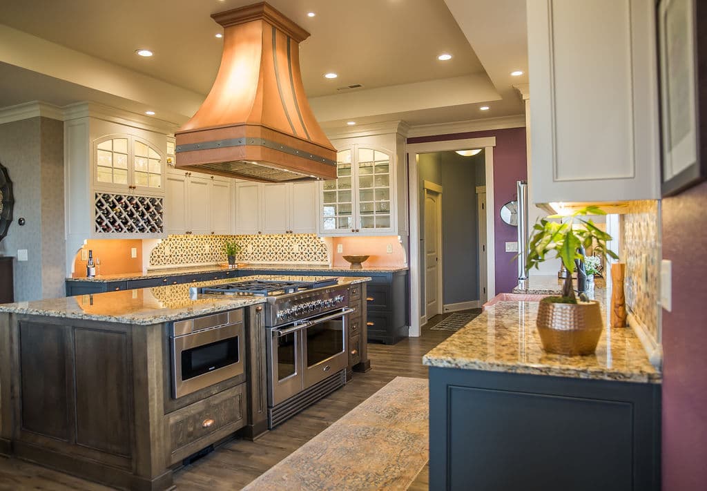 Modern kitchen with copper range hood, granite island, and elegant cabinetry.