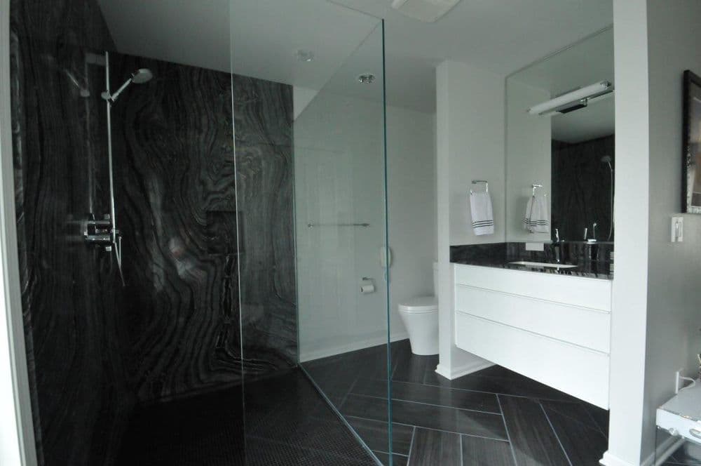 Modern bathroom with glass shower, dark marble walls, and sleek white cabinetry.